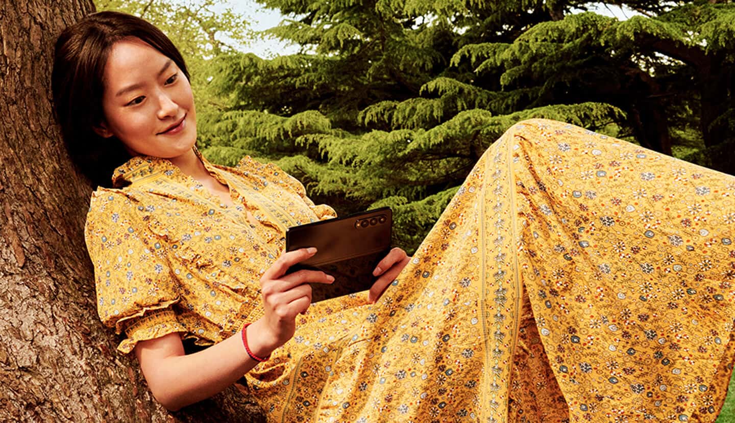 A smiling person wearing a yellow dress, using the Samsung Galaxy Z Fold 3.