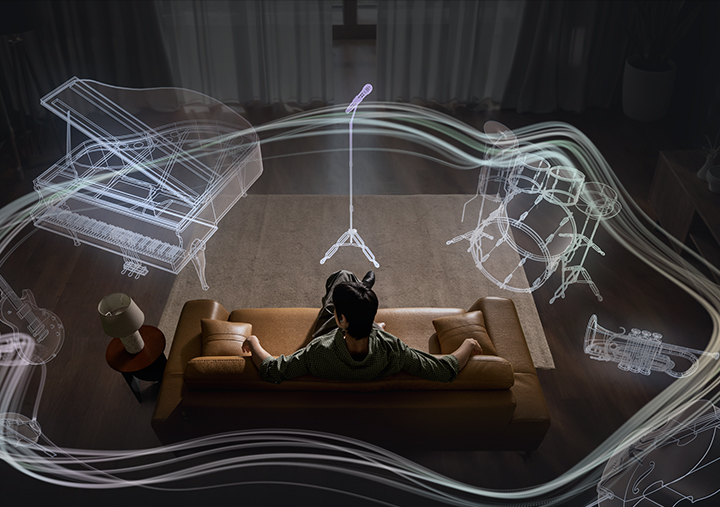 A man sitting on a couch as a collection of instruments appear in a circle around him. The instruments include a mic with a mic stand, a drum set, trumpet, cello, violin, electric guitar and grand piano. The instruments are shown in outline, highlighting the 360 Audio system available on Galaxy Buds4 Pro.