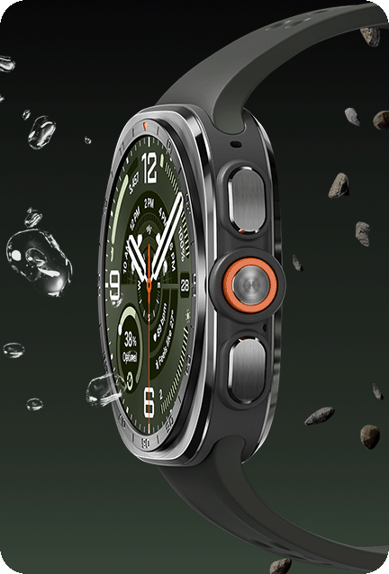 Galaxy Watch Ultra2 in Titanium Silver with an Olive Marine Band, seen from the side with water splashes and scattered sand and gravel surrounding the watch to demonstrate its rugged durability against elements such as water and dust.